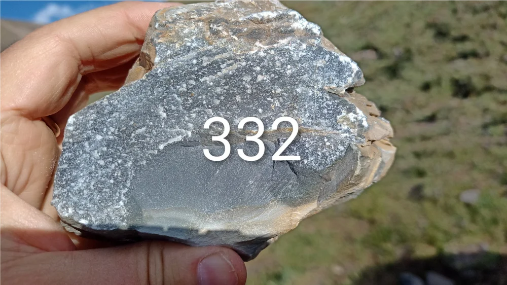 Sample G2R-332 held up against the property sky, 326 ppm Cu