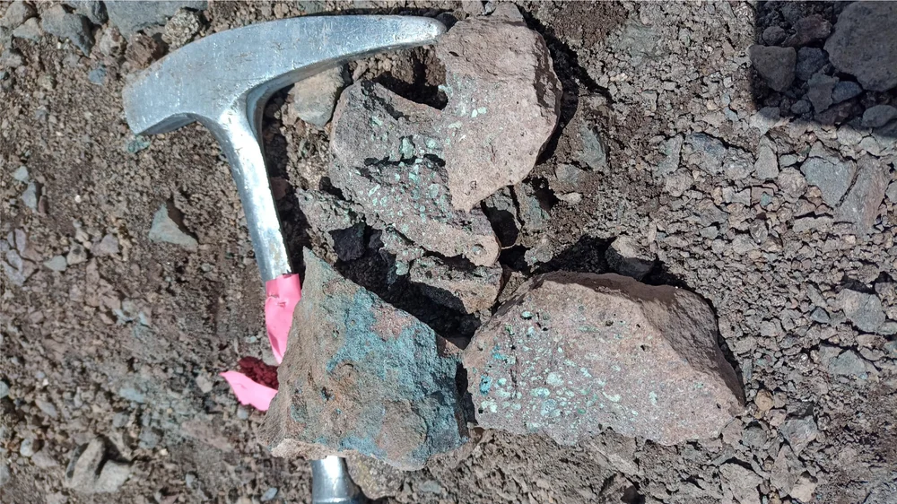 Copper-mineralised rock outcrop with rock hammer for scale, Las Estrellas northern zone